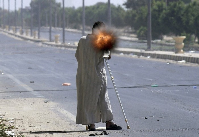 Một thành viên của phe nổi dậy chống nạng đứng bắn súng phóng lựu về phía thành Sirte.